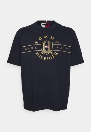 T-shirt Tommy Hilfiger bleu marine avec logo brodé en or, chiffres romains et emblème de drapeau rouge, blanc et bleu au centre de la poitrine.