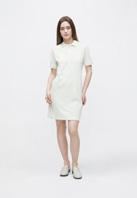 Polo obleka v svetlo bež barvi, kratki rokavi, raven kroj, narejena iz mehke tkanine, z ovratnikom in minimalističnim dizajnom. Gladek tekstura.