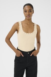 Top tank a costine color crema con scollatura ampia, accentuato da borchie metalliche lungo le spalline; abbinato a pantaloni neri a vita alta.