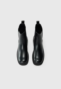 Botas negras de cuero hasta el tobillo con un acabado suave, paneles laterales elásticos y tiradores en el talón, con punta redondeada y suela plana.