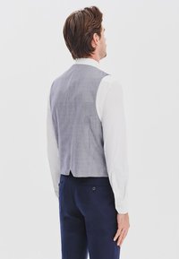 Szary i biały kamizelka w wzory o dopasowanym kroju, noszona na białej koszuli. Granatowe spodnie widoczne w pasie, gładka struktura tkaniny.