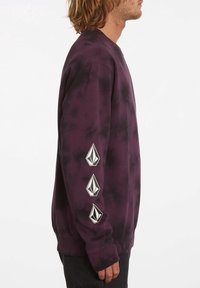 Lila tie-dye sweatshirt med långa ärmar. Har tre vita logotypdetaljer längs vänster arm. Ribbad mudd och nederkant. Mjuk tygtextur.