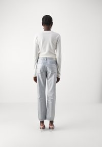 Jeans gris claro de corte recto, con bolsillos traseros y costuras sutiles, combinados con una camiseta blanca de manga larga.