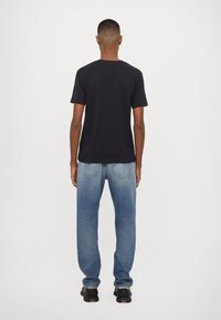 Schwarzes T-Shirt mit kurzen Ärmeln, von hinten betrachtet, kombiniert mit hellblauen Jeans und schwarzen Sportschuhen. Einfaches Design, lässige Passform.