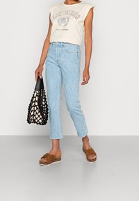 Ljust blå randiga jeans med avsmalnande ben, tillsammans med en beige ärmlös topp och bruna plattformssandaler. Håller en svart och krämfärgad nätv äska.