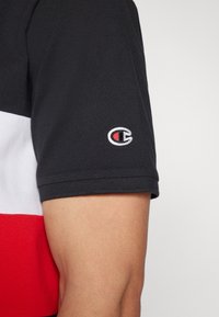 Schwarzes Poloshirt mit roten und weißen horizontalen Streifen, strukturiertem Stoff und kleinem gesticktem Logo auf dem linken Ärmel.
