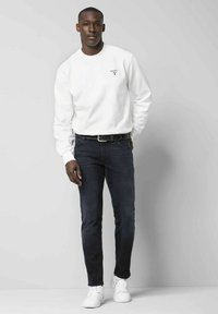 Weißer Pullover mit Logo, dunkle Jeans und weiße Sneakers. Glattes Material und taillierte Passform mit einem einfachen, modernen Look.