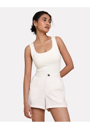 Witte aansluitende tanktop met brede banden, gecombineerd met lichtbeige high-waisted shorts met een voorknop en zijzakken.
