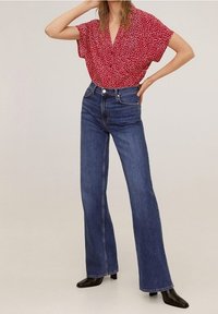 Rode blouse met korte mouwen en witte stippen, gecombineerd met donkerblauwe hoge flared jeans en zwarte puntige enkellaarsjes.