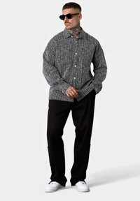 Schwarz-weiß gestreiftes Hemd mit Knöpfen und Kragen, strukturierter Stoff, zwei Taschen; kombiniert mit schwarzen Hosen und weißen Sneakers.