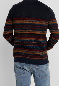 Pull en tricot avec une base bleu marine et des rayures horizontales multicolores en orange, rouge et turquoise, texturé avec différents motifs.