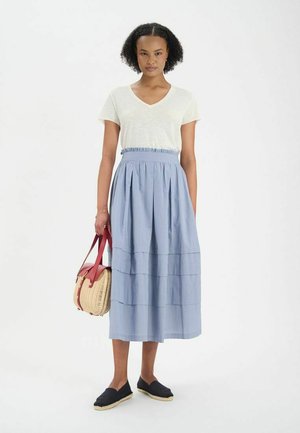T-shirt blanc en V, jupe midi rayée bleue avec un design à volants, chaussures espadrilles noires et un sac en osier avec des accents rouges.