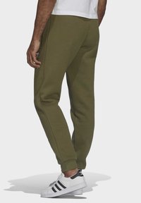 Gröna bomulls-joggers med sidofickor, elastiska muddar och diskret logodetalj på låret, kombinerade med vita sneakers med svarta ränder.