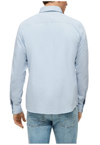 Camicia azzurra a maniche lunghe in cotone, con colletto classico e polsini con bottoni. Indossata con jeans in denim blu, che mostrano una vestibilità casual.