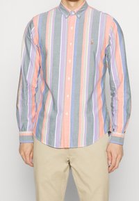 Knapplång skjorta med vertikala ränder i rosa, grått, lavendel och ljusblått. Har en spetsig krage och en liten logotyp på bröstet.