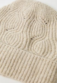 Crème-kleurige gebreide wollen beanie met een geribde manchette en een textuur met kabels in een close-upweergave.