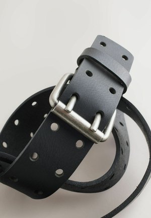 Sort læderbælte med en struktureret overflade, der har en metalspænde og flere huller til justering. Det er let snoet, hvilket viser dets fleksibilitet.