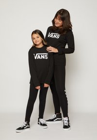 Sorte langærmede skjorter og leggings med hvid "VANS" logo; parret med sorte høje sneakers, der viser en afslappet og matchende stil.