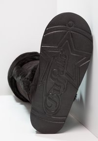 Svart faux fur stövlar med en texturerad gummisula som har en stjärndesign. Den övre delen är mjuk och fluffig, vilket ger värme och komfort.