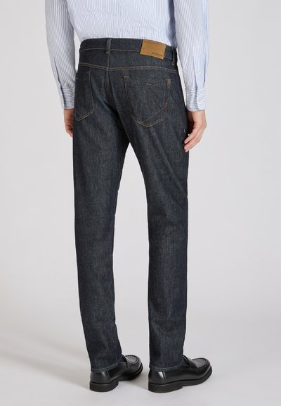 Jean en denim bleu foncé avec une coupe droite, des coutures discrètes et une étiquette en cuir sur la taille arrière. Comprend deux poches à l'arrière.