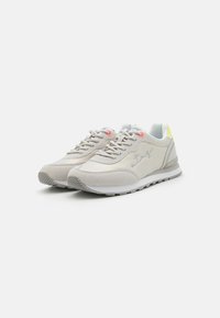Baskets de sport gris clair avec un mélange de cuir lisse et de daim, design à lacets, branding subtil et accents contrastés en orange et jaune.