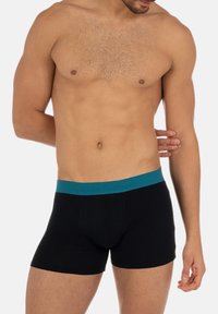 Boxer neri con una cintura elastica turchese, con un logo impressa sulla parte anteriore. Il tessuto sembra liscio e aderente.