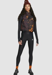 Dopasowane czarne legginsy w połączeniu z bezrękawnikem w marmurkowy wzór w odcieniach fioletu i pomarańczy. Dodatki to pomarańczowa czapka.