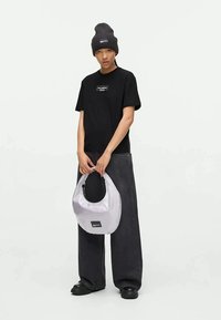 T-shirt de algodão preto com logótipo, jeans cinzentos oversized, gorro de malha cinzento e uma bolsa semi-transparente branca com um retalho preto e fecho.
