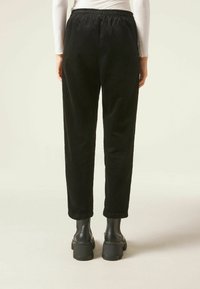 Pantalon en velours côtelé noir à coupe décontractée, taille élastique et chevilles retroussées, associé à des bottes plateformes noires épaisses.