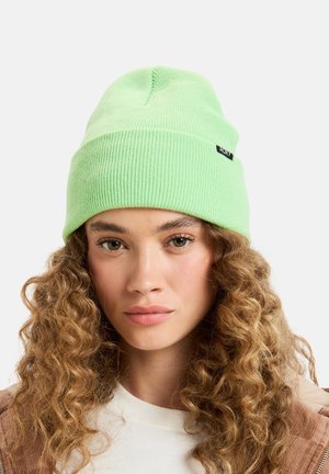 Green ribbed beanie hat made of soft fabric, featuring a small black brand tag on the side. The design is fitted and snug.