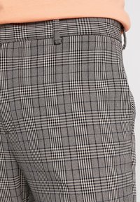 Pantalons à carreaux noir et blanc avec un tissu texturé. Présente des motifs de carreaux nets et distincts ainsi qu'une coupe ajustée à la taille.