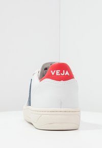 Baskets blanches avec semelle beige, languette de talon rouge indiquant "VEJA" et bande latérale bleu marine, vues de dos sur fond blanc.