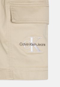 Bežna tkanina s glatkom teksturom ima zakrpa džep i izvezeni logo "Calvin Klein Jeans", pri čemu je "CK" istaknut u bijeloj i srebrnoj boji.