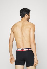 Melni bokseršortai ar baltu, zilu un sarkanu svītru jostu, uz kuras redzams Levi's logos; modelis attēlots no aizmugures, redzama neapstrādāta āda.