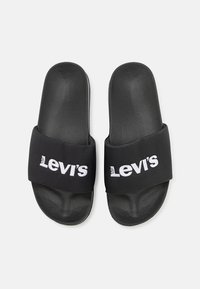 Sandales noires à semelle texturée et large bride avec le logo blanc de Levi's affiché de manière proéminente. Fabriquées en matériaux synthétiques.