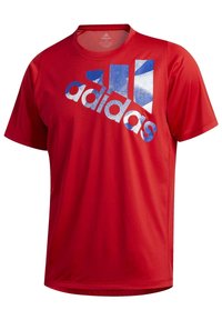 T-shirt de sport rouge à manches courtes avec un col rond et un grand logo Adidas bleu et blanc sur la poitrine.