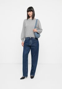 Suéter de punto gris con mangas largas ligeramente abullonadas, combinado con jeans de mezclilla azules holgados y bailarinas negras con punta. Bolsa de hombro azul claro.
