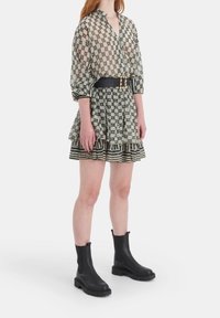 Mönstrad klänning med en åtdragen svart bälte, volangkant och genomskinliga långa ärmar. I kombination med svarta stövlar vid vristen.