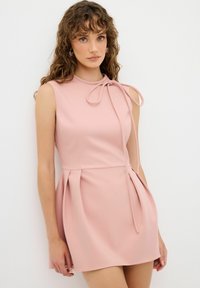 Robe courte rose en tissu lisse, dotée d'un corsage ajusté, d'une jupe plissée et d'un détail de col noué.