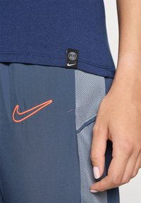 Marineblå bomull T-skjorte med svart Paris-logo etikett, kombinert med grå treningsshorts som har et mesh-panel og oransje Nike swoosh detalj.