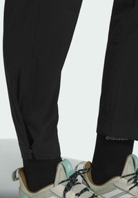 Pantalones ligeros negros con un diseño ajustado, combinados con zapatillas deportivas grises y menta que presentan detalles de malla y calcetines negros texturizados.