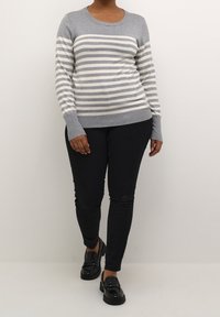 Pull rayé gris et blanc à manches longues et poignets côtelés, assorti à un pantalon noir slim et des mocassins noirs brillants.