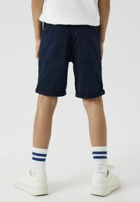 Shorts bleu marine avec des poignets retroussés, des poches arrière et une taille plate, associés à des sneakers blanches et des chaussettes blanches avec des rayures bleues.