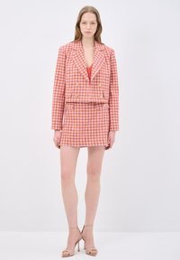 Dwurzędowa marynarka i dopasowana mini spódnica w różowo-białą kratę w stylu houndstooth. Posiada złote guziki i skrócony fason. Gładka faktura.