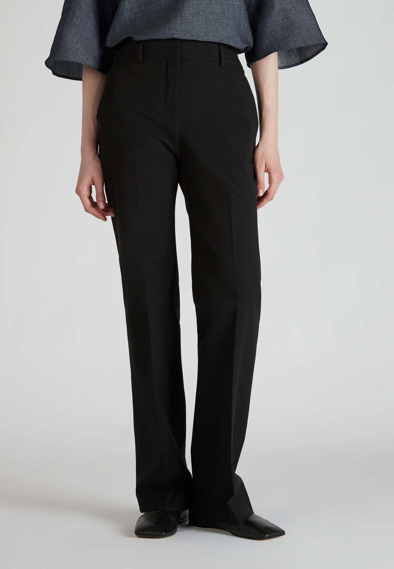Zwarte, op maat gemaakte broek met een rechte pijpdesign, zachte textuur en riemlussen. Gepaard met donkere schoenen voor een complete look.