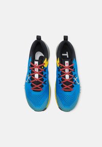 Scarpe da ginnastica blu con un design perforato, accenti gialli a contrasto, lacci rossi e una fodera interna nera. Presentano una suola grigia e un logo.