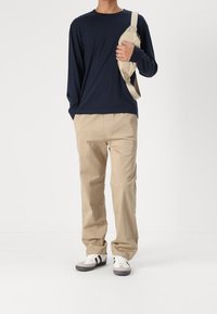Long-sleeve navy shirt, beige trousers, gray and white sneakers. Brown crossbody bag with a light strap. Clean, casual outfit design.
