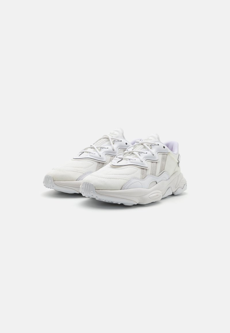 Białe sportowe sneakersy z teksturowanym materiałem górnym, warstwową konstrukcją, wyraźną miękką podeszwą i sznurowanym zapięciem.