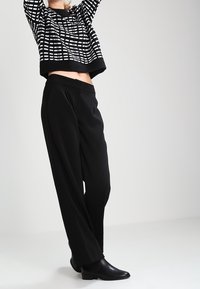 Czarnobiały sweter w paski z prążkowanym obszyciem, zestawiony z luźnymi czarnymi spodniami i eleganckimi czarnymi botkami, na tle jasnego tła.