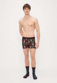 A piros kockás boxer alsónadrág ünnepi rénszarvas mintával rendelkezik, amelyhez egy kiegészítő zokni is tartozik. Mindkét termék kényelmes szabású és rugalmas derékrésszel rendelkezik.